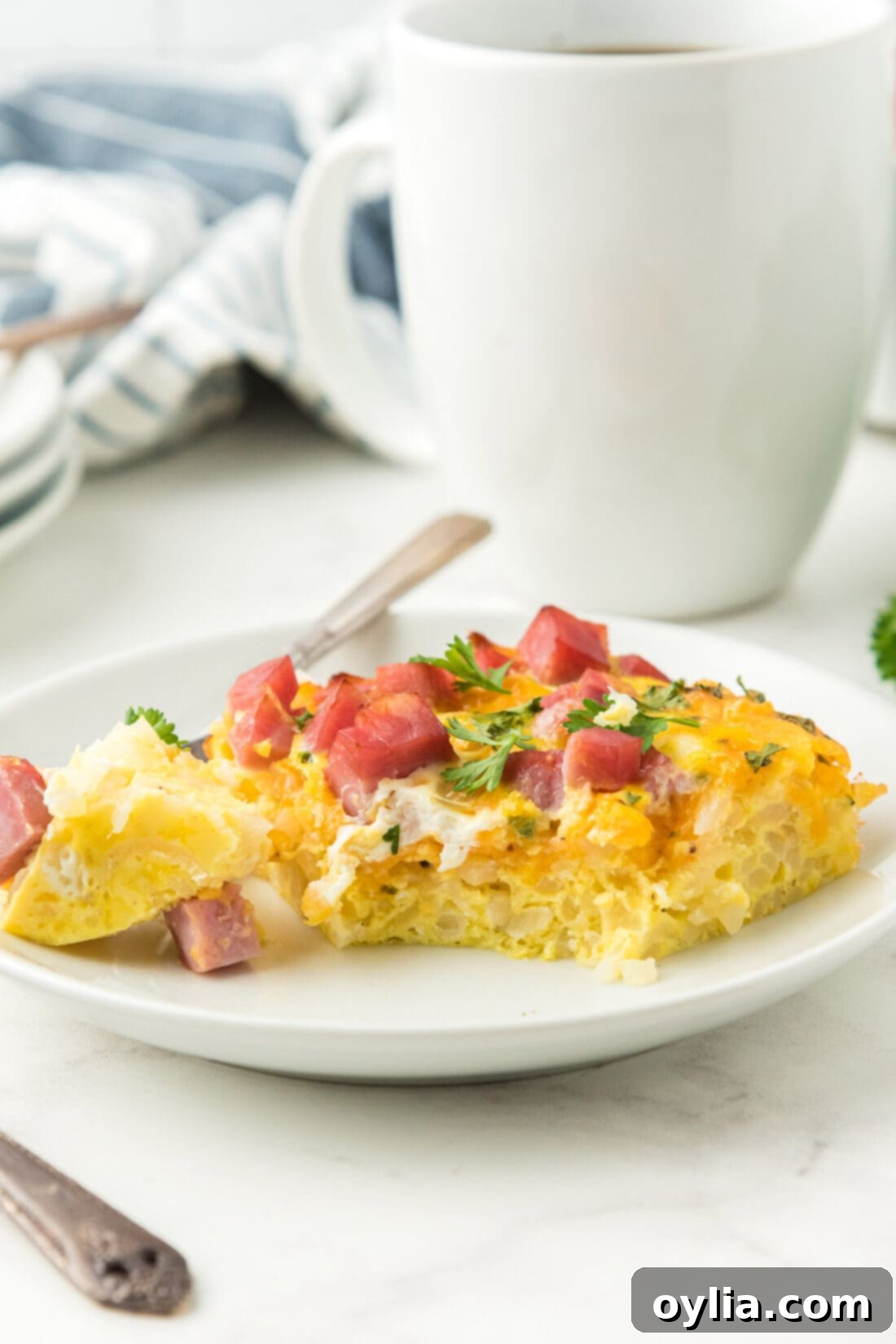 Breakfast casserole on a plate, showing a slice with layers of ham, cheese, and hash browns