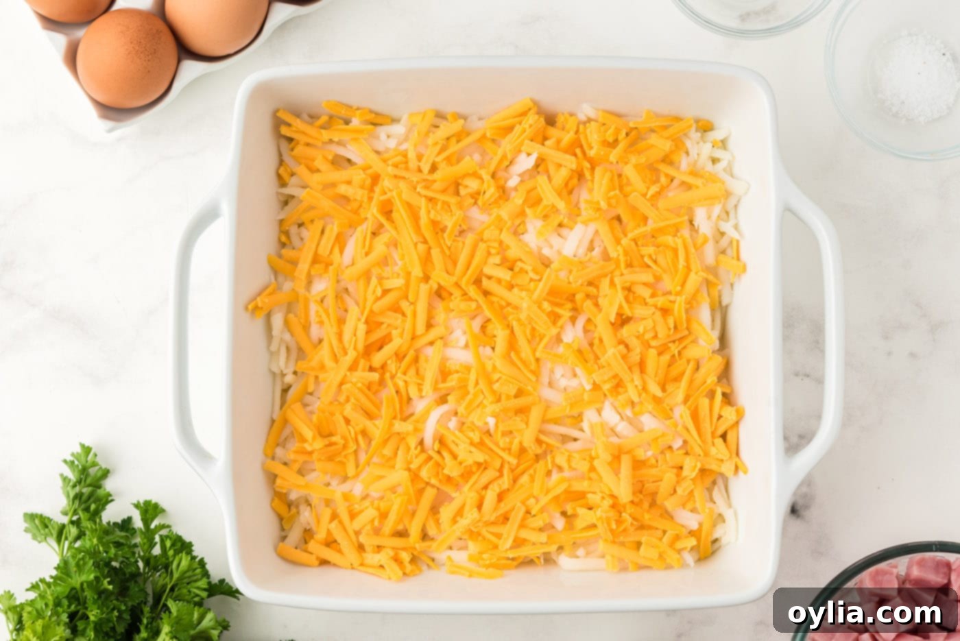 Shredded cheddar cheese layered over hash browns in a baking dish