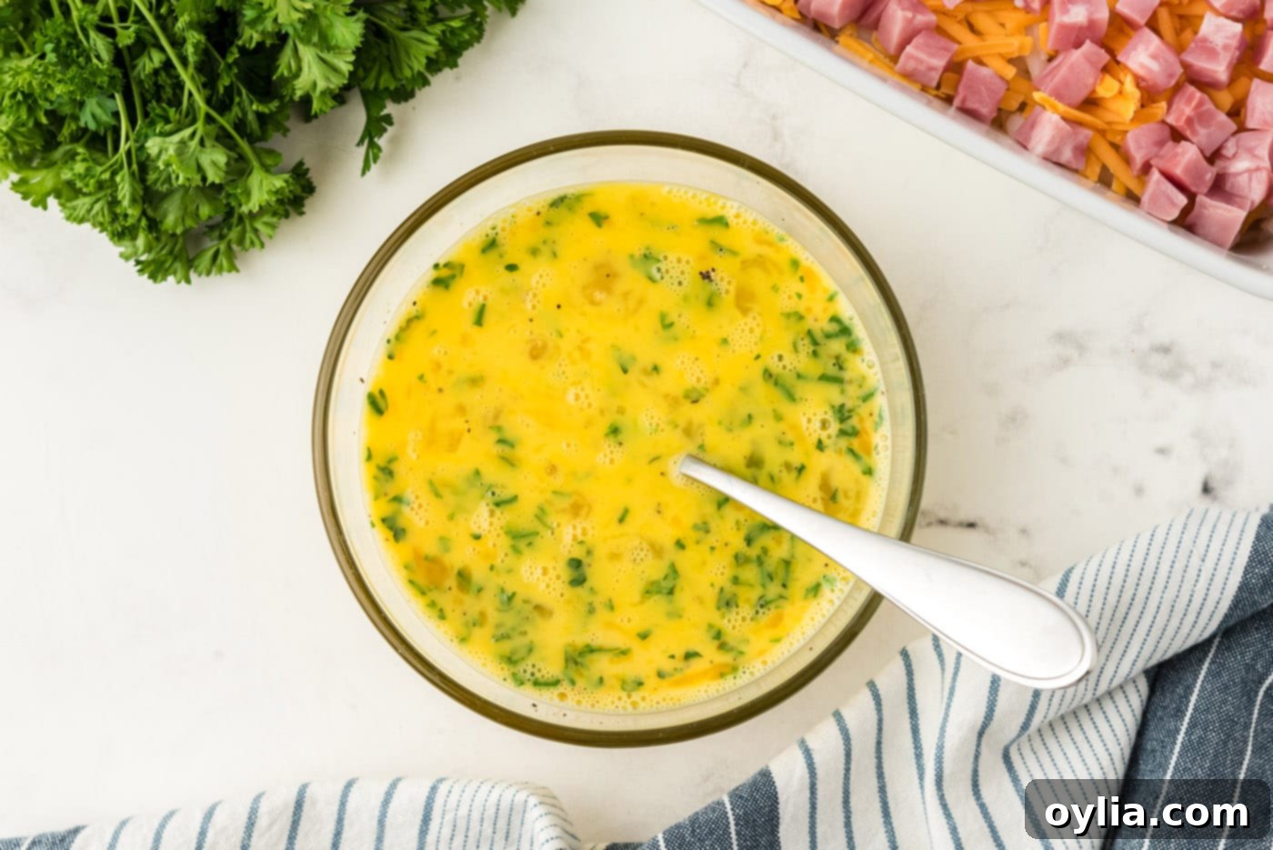 Egg mixture with milk, seasonings, and parsley in a mixing bowl