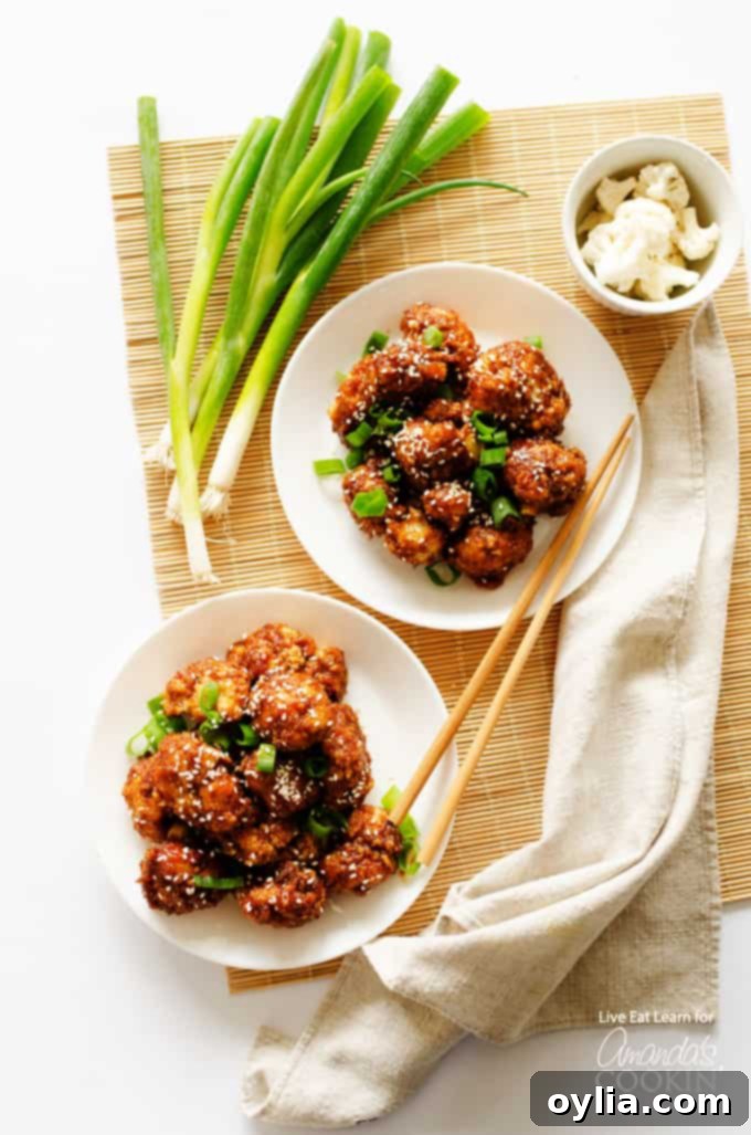 Two servings of sticky garlic cauliflower garnished with green onions and sesame seeds, ready to eat.