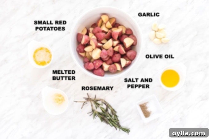 Ingredients for making roasted potatoes: small red potatoes, whole and minced garlic cloves, melted butter, olive oil, fresh rosemary sprigs, Kosher salt, and black pepper displayed on a wooden board
