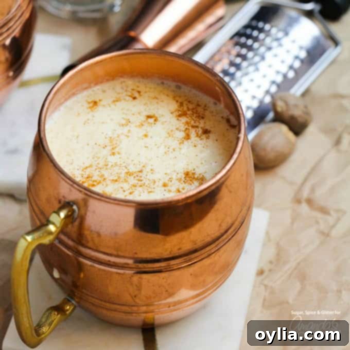 A close-up of a classic copper mug overflowing with creamy, perfectly spiced homemade eggnog.