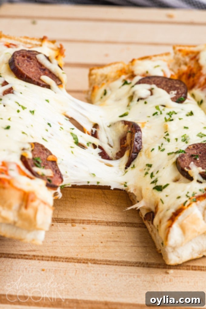 Melted mozzarella cheese pulling apart from a slice of French bread pizza.