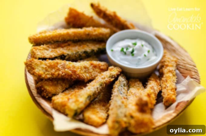 A plate of crispy baked zucchini fries with a small bowl of creamy gorgonzola dipping sauce, garnished with fresh chives.