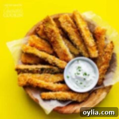 A vibrant close-up of crispy zucchini fries, perfectly golden, served with a creamy dip in a bowl.