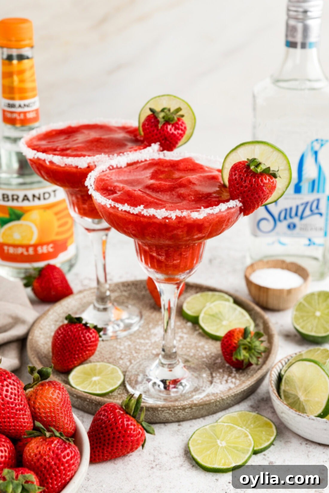 Two Strawberry Margaritas on a serving platter surrounded by limes and strawberries