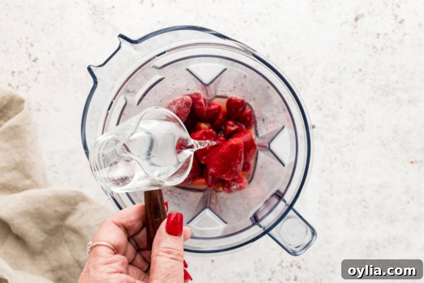 hand pouring silver tequila over top frozen strawberries in a blender