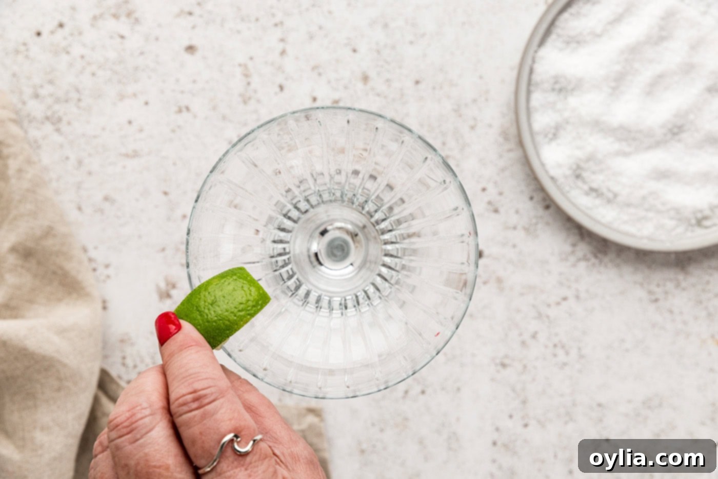 hand rubbing a lime wedge over the rim of a margarita glass