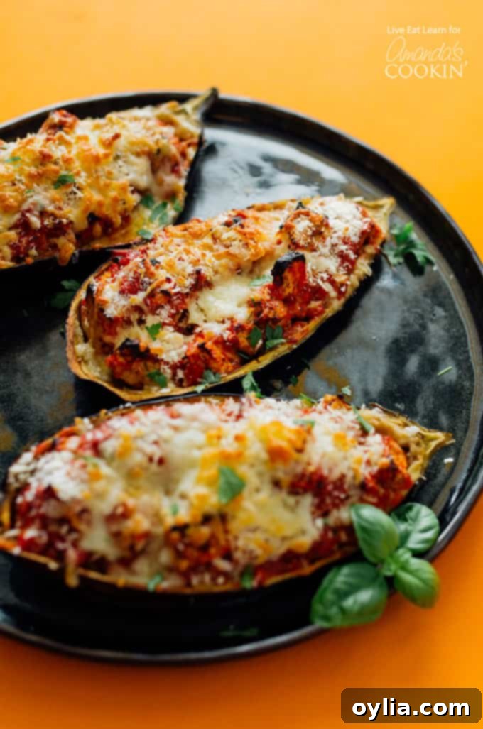 Two halves of cooked Stuffed Baked Eggplant Parmesan on a black plate, garnished with fresh basil, showcasing melted cheese and a crispy topping.