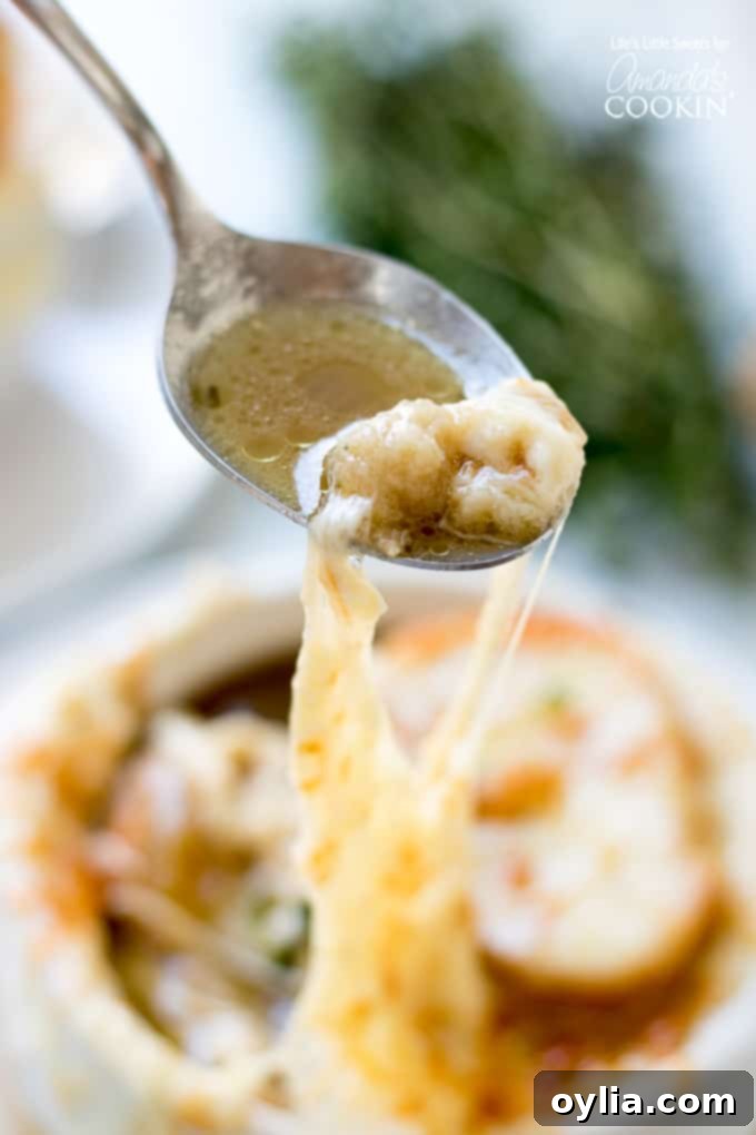 A close-up of a spoon pulling a long string of melted cheese from a bowl of French Onion Soup.