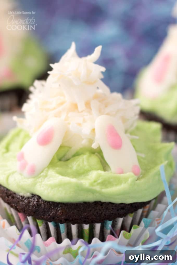 Fully decorated Bunny Butt Cupcake with chocolate feet, marshmallow body, and coconut tail on a green frosted chocolate cupcake.