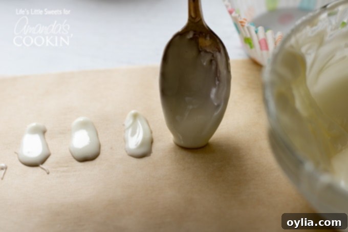 Spoon creating white chocolate oval shapes on parchment paper on a baking sheet to form bunny feet.