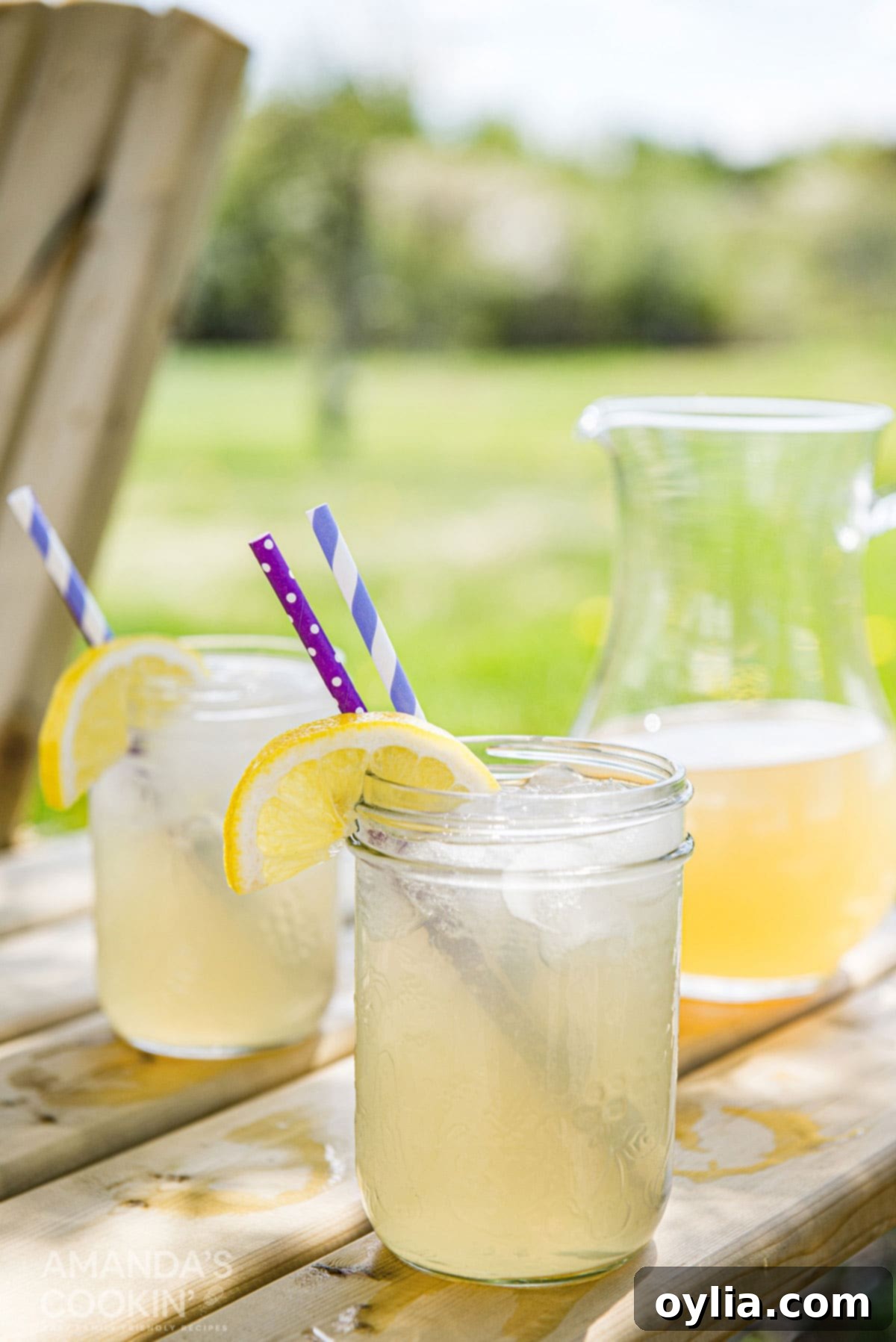 Serve this Jack Daniel's spiked Lynchburg Lemonade at your next backyard party or enjoy a refreshing glass on the porch. A pitcher of Lynchburg lemonade and two mason jars resting on a picnic table. Mason jars have a wedge of lemon and a straw in each glass.