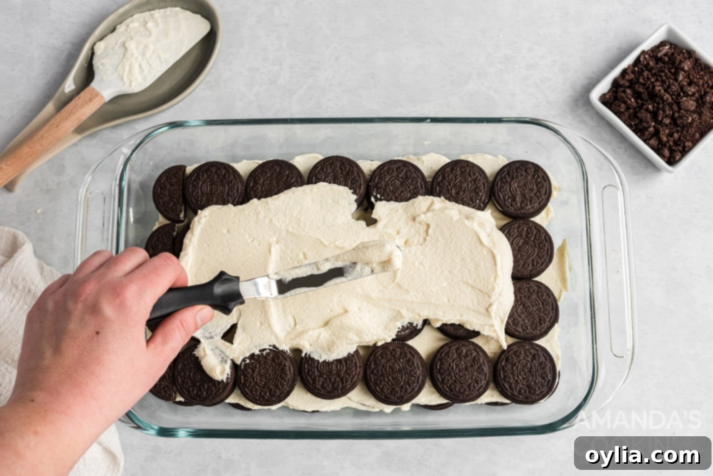 spreading whipped topping over the top of oreos in a baking dish