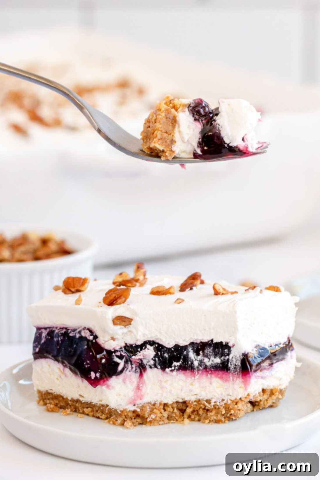 Forkful of Blueberry Delight held above a slice of Blueberry Delight, showcasing the beautiful layers of crust, cream cheese, blueberry, and whipped topping.