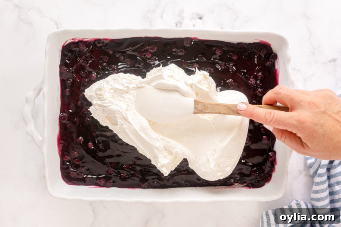 Spreading the final layer of whipped topping over the blueberry pie filling.