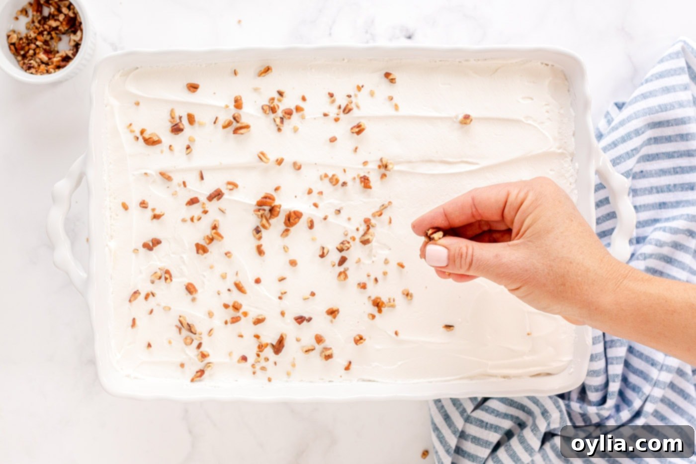 A hand sprinkling chopped pecans as a garnish on top of the whipped topping.