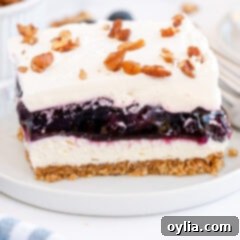 Delicious Blueberry Lush, a layered dessert with a graham cracker pecan crust, cream cheese, blueberry pie filling, and whipped topping.
