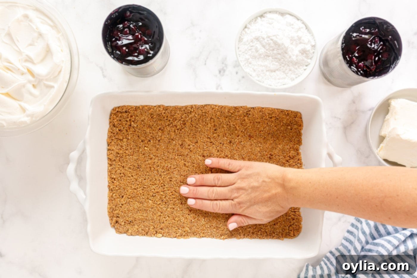 Pressing the graham cracker crust mixture firmly into a 13x9 inch pan before baking.