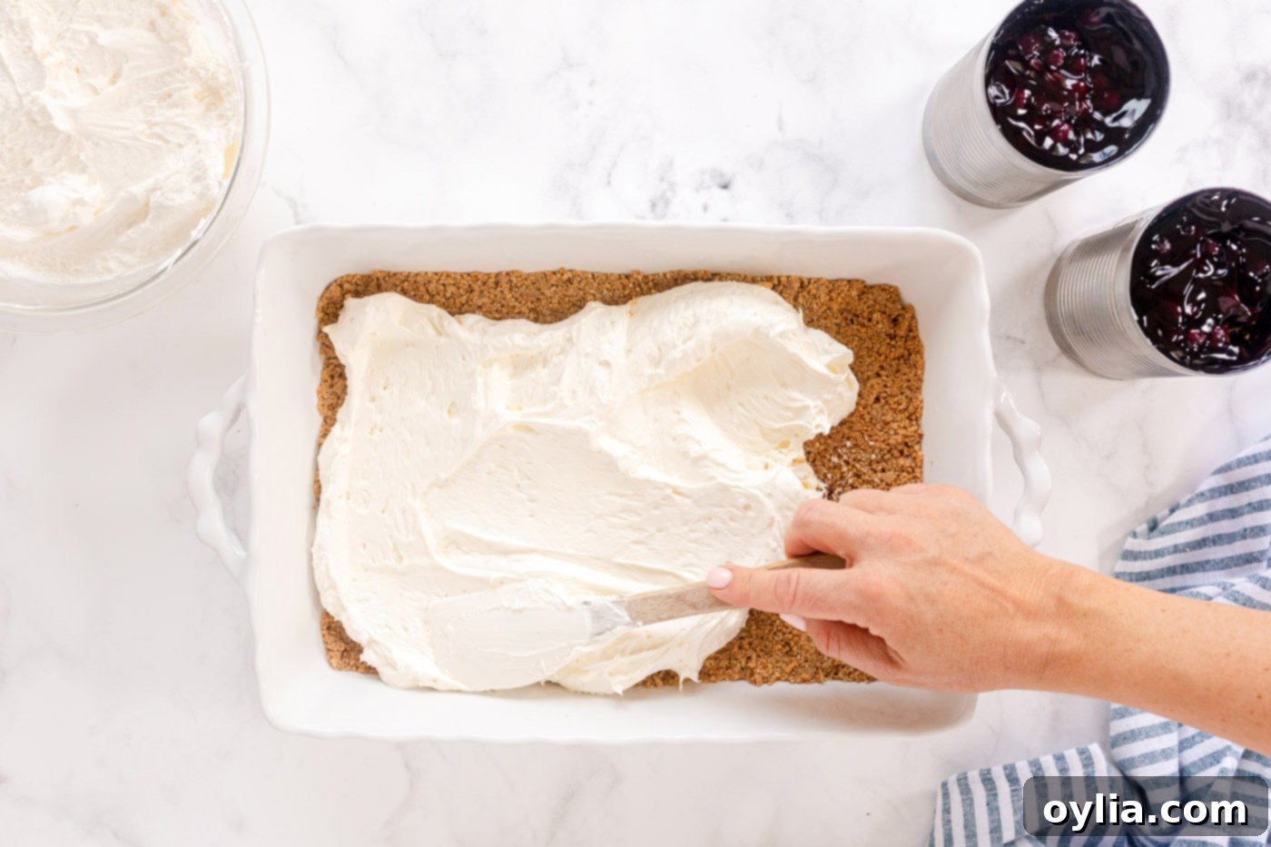 Spreading the smooth cream cheese layer evenly over the baked graham cracker crust.