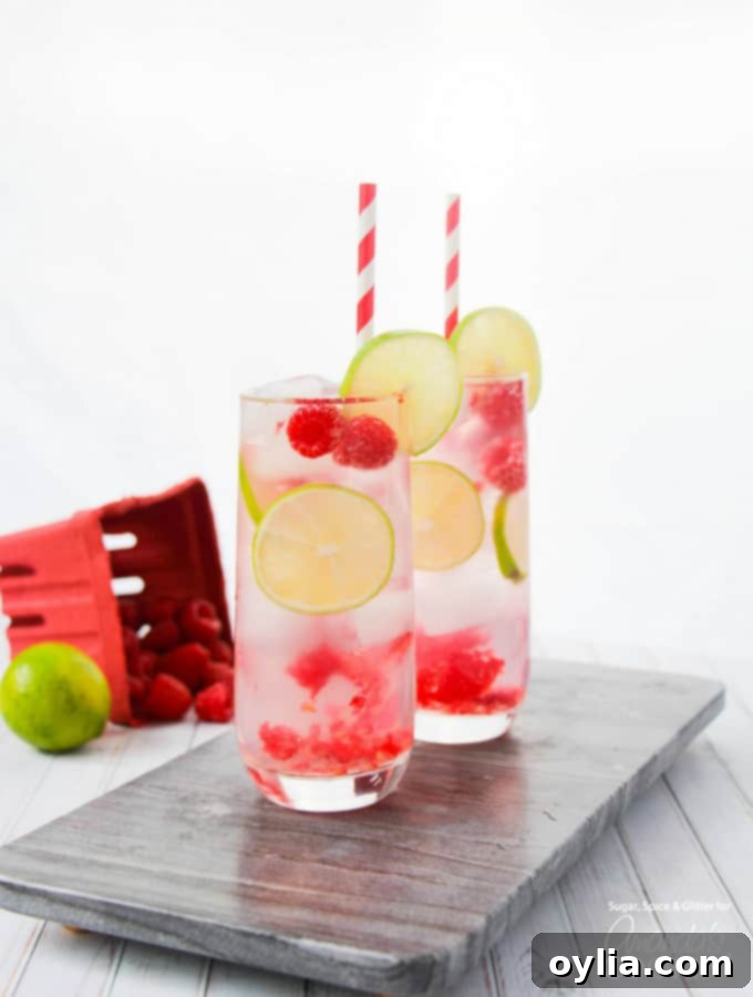 Cocktail in glass with paper straws, lime, and raspberries