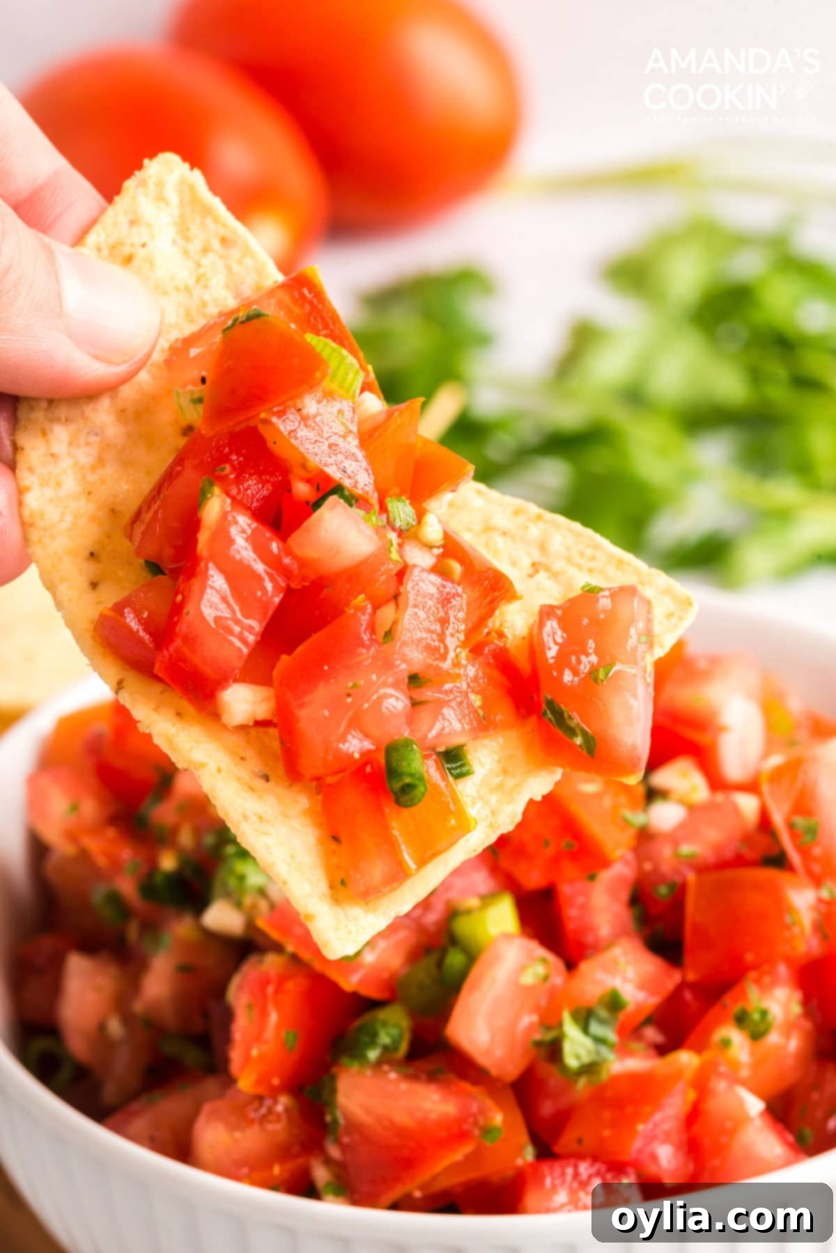 hand lifting tortilla chip with salsa fresca on it