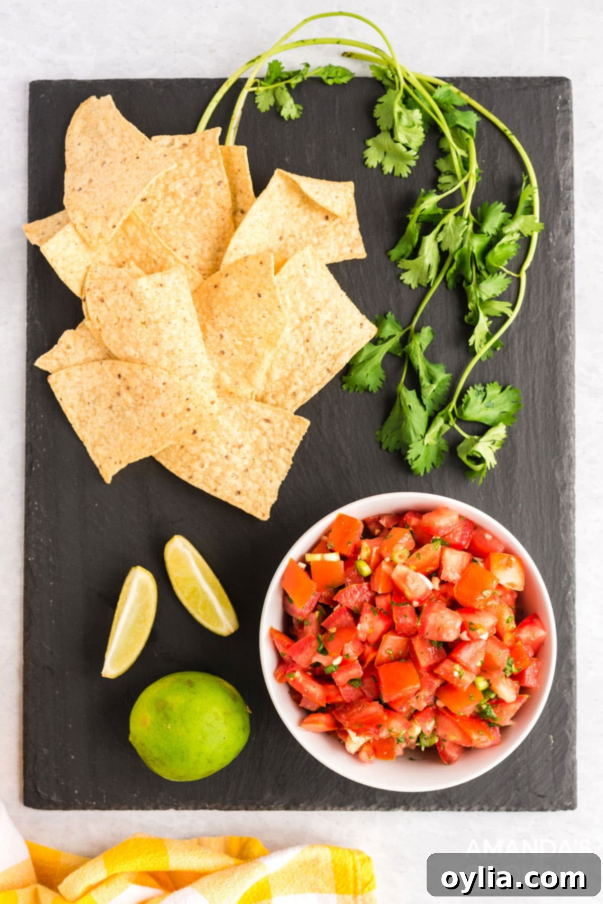 bowl of salsa fresca on a black board with chips, cilantro, and limes