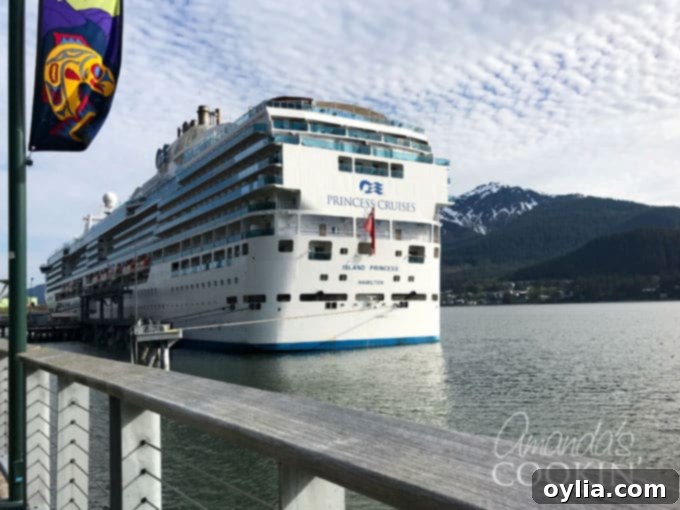 The Island Princess cruise ship docked in Juneau, Alaska, against a scenic backdrop