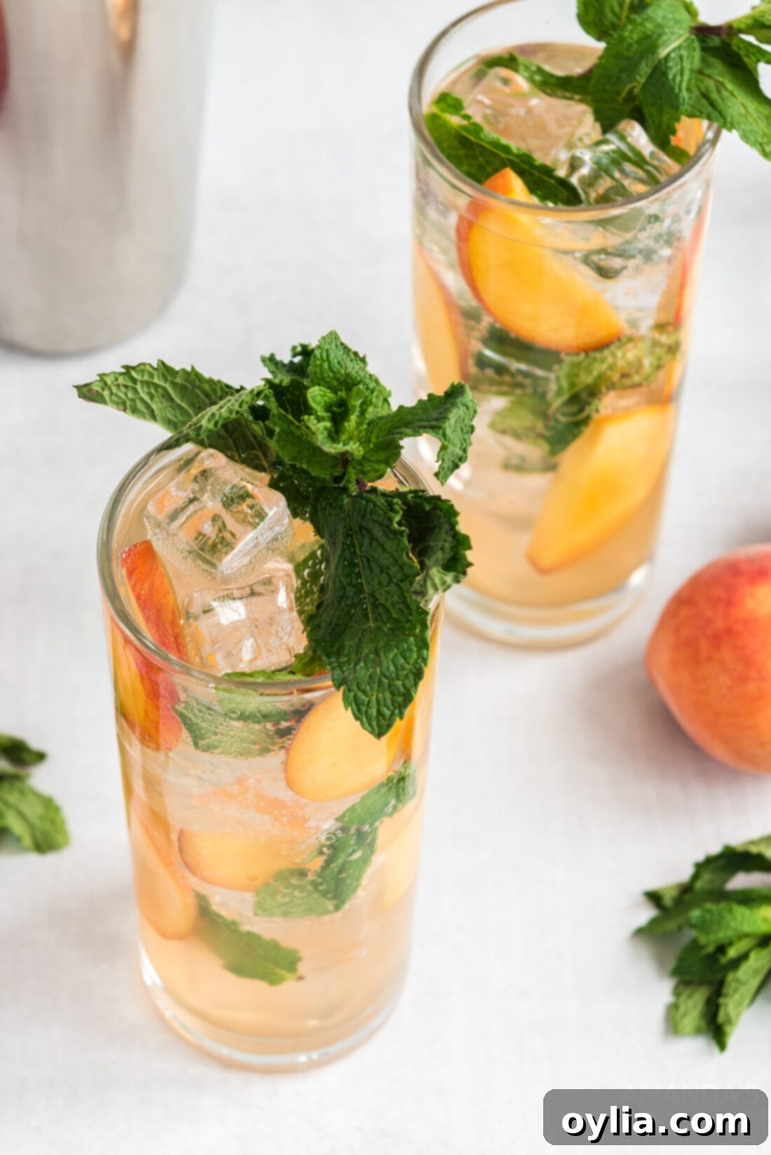 Two tall glasses filled with peach mojitos, featuring peach slices, mint leaves, and ice, ready to be enjoyed.
