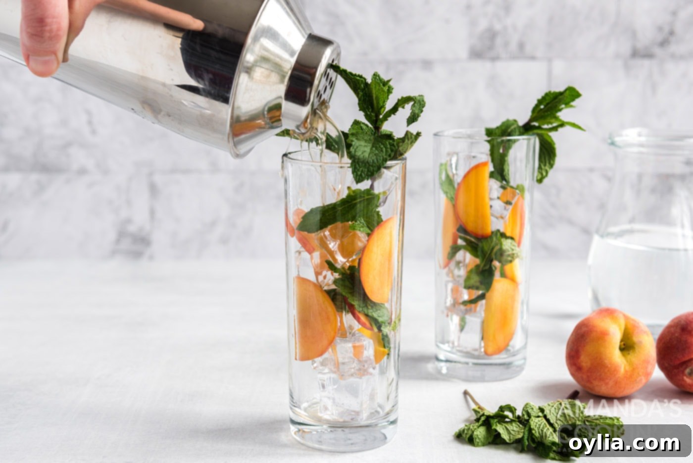 Pouring the peach-infused rum from a cocktail shaker into a glass filled with ice, mint, and peach slices.