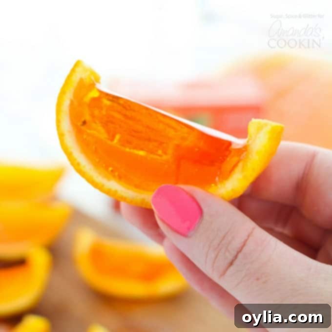 A close-up of a partially sliced orange jello shot, showing the vibrant orange jello perfectly set within the orange rind, on a wooden cutting board.