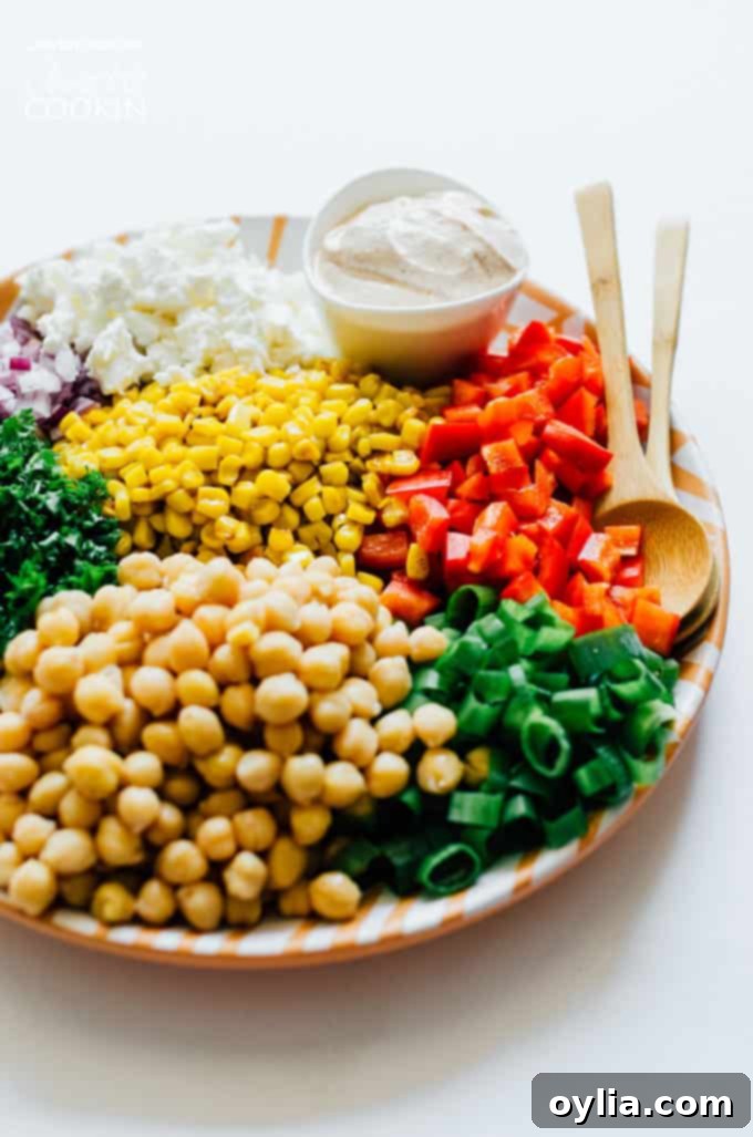 Fresh ingredients for sweet corn and chickpea salad laid out on a white plate, including corn, chickpeas, red bell pepper, and parsley.