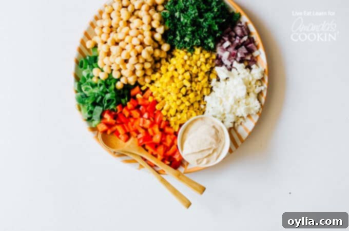 A vibrant close-up of sweet corn and chickpea salad with fresh herbs and bell peppers, on a white plate, ready to be enjoyed.