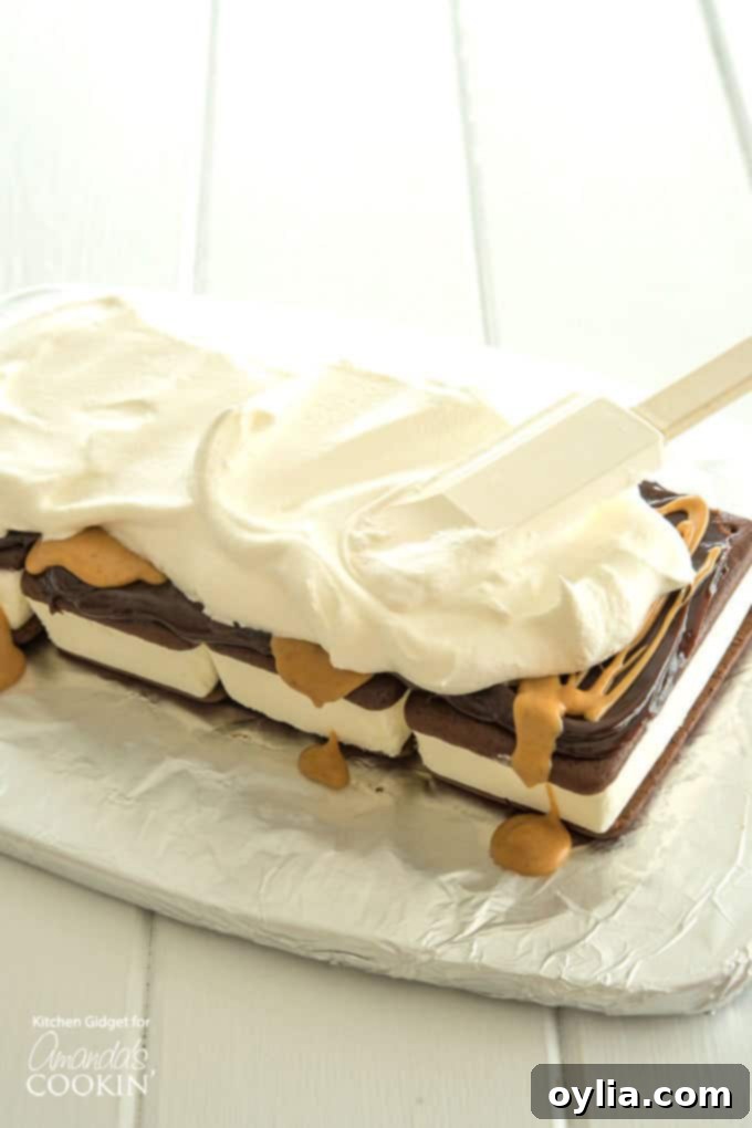 Smooth whipped topping being spread evenly over the fudge and peanut butter layer of the ice cream sandwich cake.