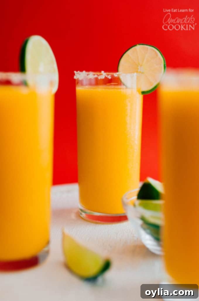 Three glasses full of mango margarita slush with a lime garnish