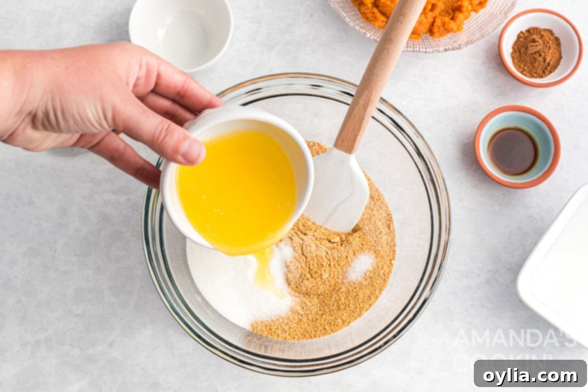 Melted butter being poured over graham cracker crumbs in a mixing bowl for the cheesecake crust.