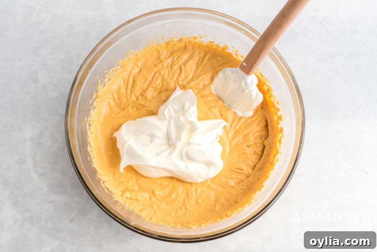 Whipped topping gently folded into the smooth pumpkin cheesecake batter in a mixing bowl.
