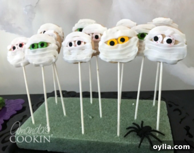 Halloween mummy cookies with white icing bandages and bloodshot candy eyes, presented on a plate.