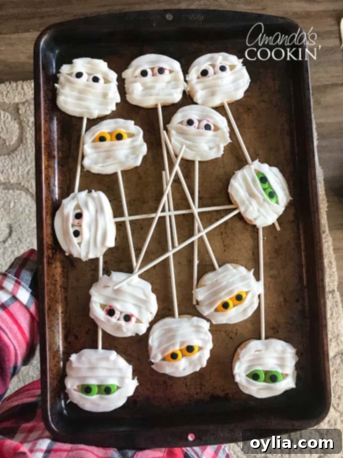 Mummy cookies on lollipop sticks, displayed in floral styrofoam, ready for a Halloween party.