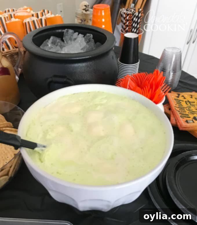 A vibrant green Halloween punch, garnished with gummy worms, in a large punch bowl, ready to serve as a spooky non-alcoholic drink.