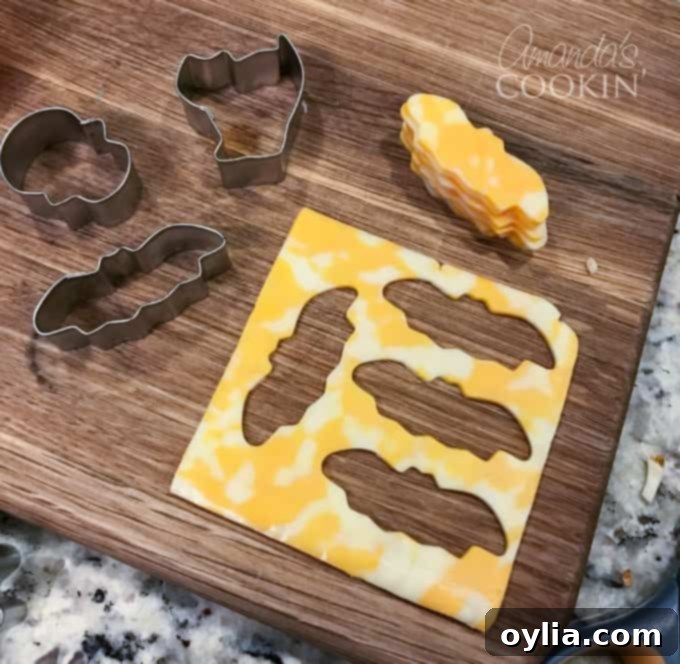 Close-up of Halloween cookie cutter cheese shapes, featuring ghosts, pumpkins, and bats, on a serving platter.