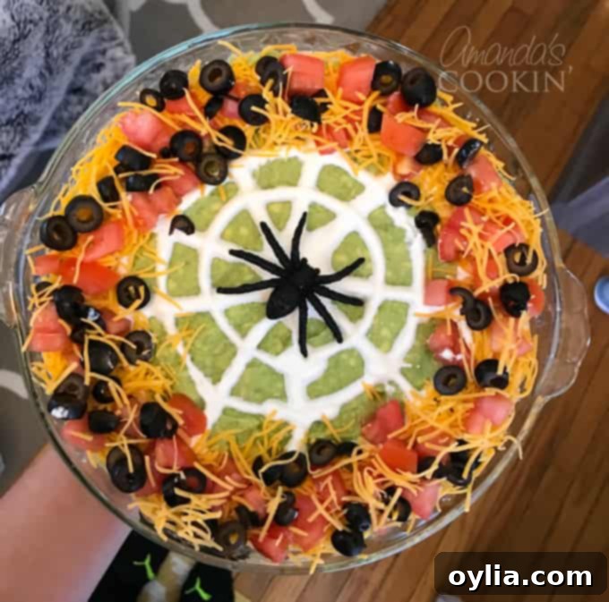 A spooky spider web taco dip in a serving dish, garnished with a sour cream web and black olive spider, ready for dipping.