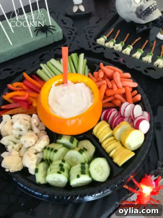Fresh vegetables arranged around a hollowed-out pumpkin filled with dip, an inviting and healthy Halloween appetizer.