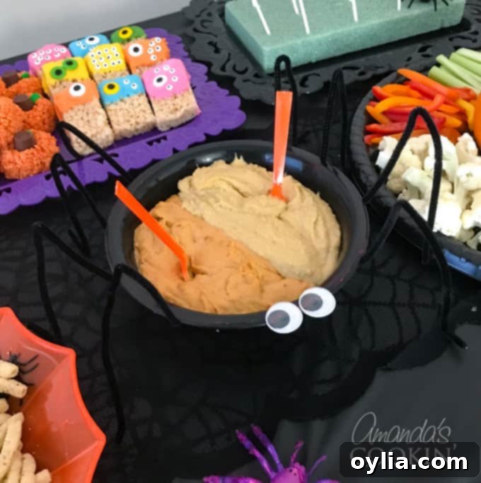 A black spider bowl filled with hummus, garnished with black olive 'spider' decorations and googly eyes, serving as a creative Halloween food idea.