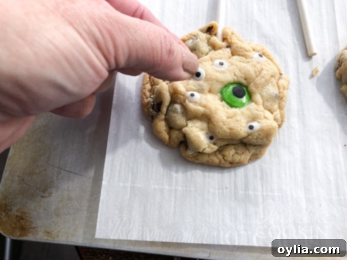 Adding candy eyeballs to freshly baked cookie pops for a monster effect