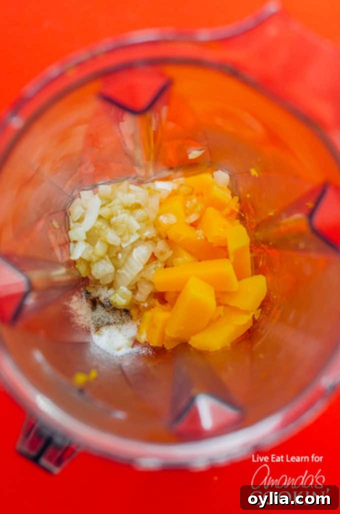 Close-up shot of the ingredients for Butternut Squash Mac and Cheese being pureed directly in a pot with an immersion blender, creating a smooth, orange sauce.