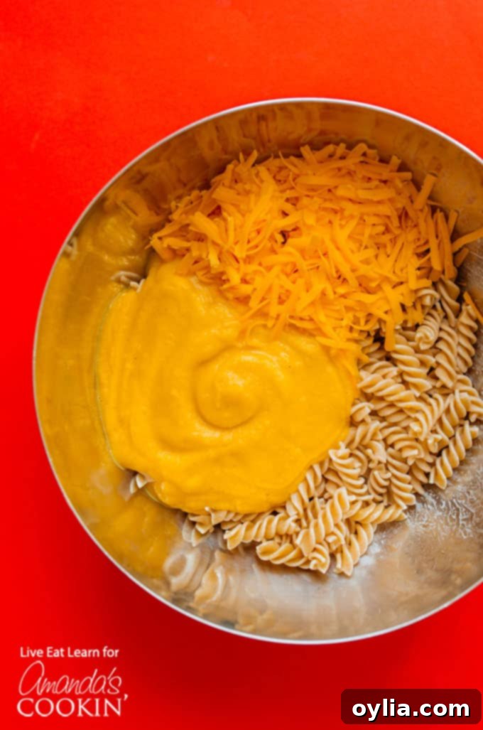 All the fresh ingredients for Butternut Squash Mac and Cheese laid out on a wooden cutting board, including diced squash, onion, garlic, pasta, and cheese.