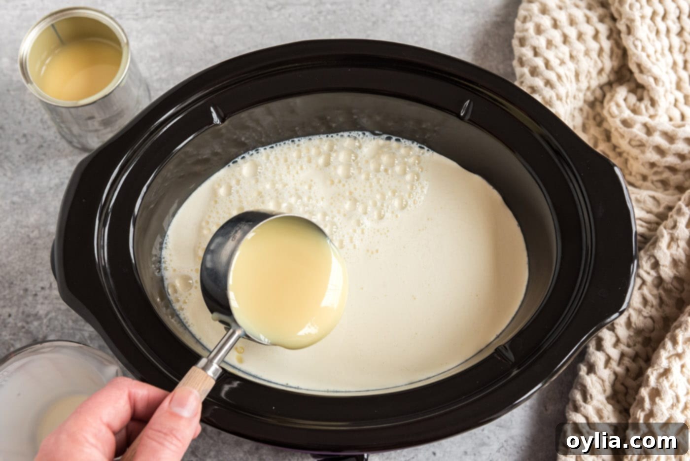 pouring sweetened condensed milk into crockpot with heavy whipping cream