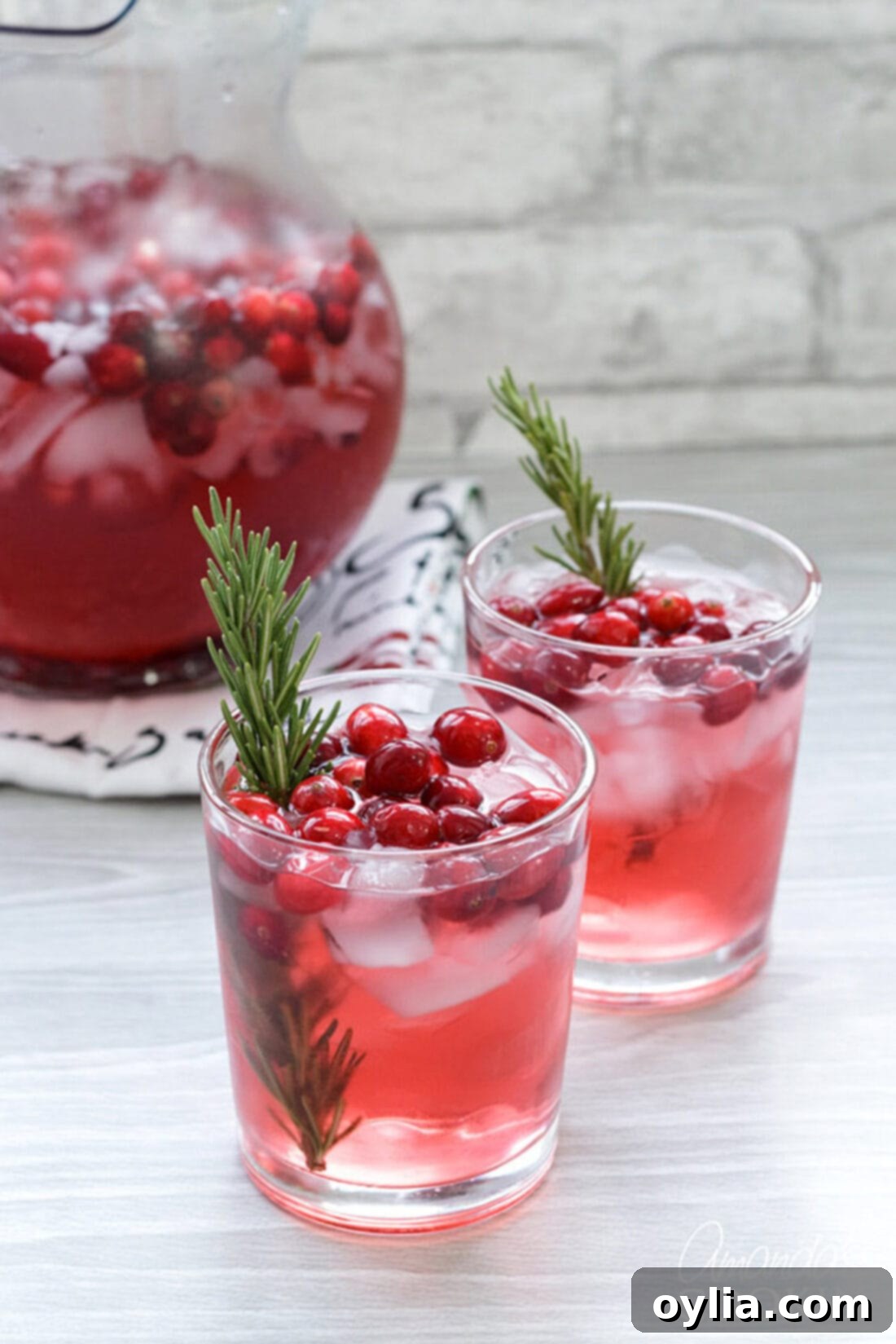Close-up of cranberry holiday punch with rosemary sprigs as garnish in a glass pitcher, showcasing its vibrant red color.