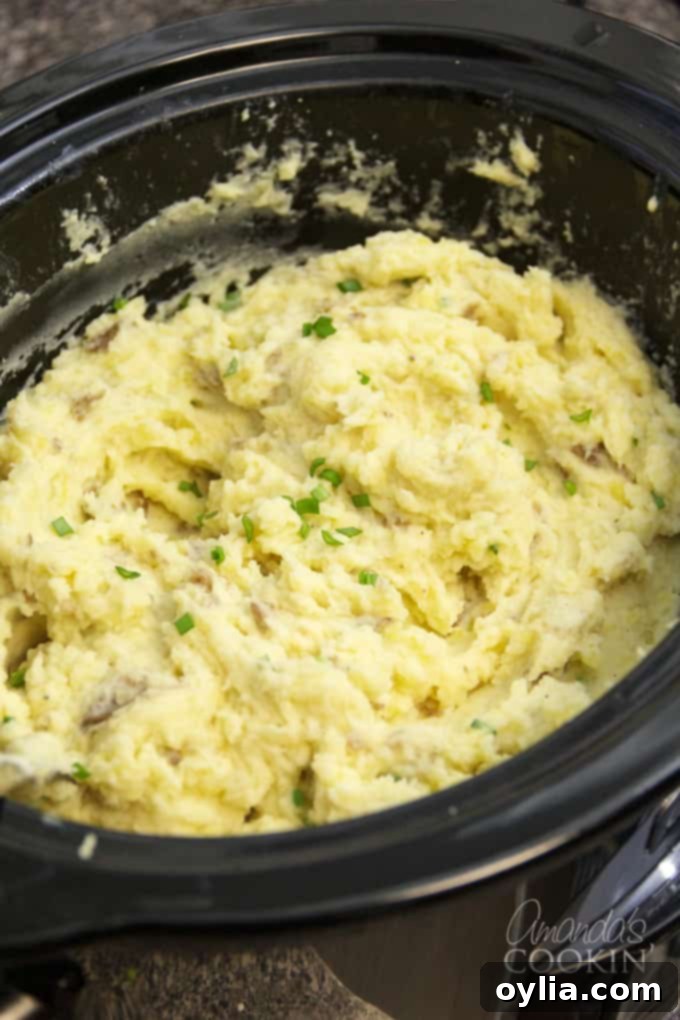 These Crockpot Mashed Potatoes have the skin on, but you can peel them if you want to. Making mashed potatoes in the slow cooker is perfect for the holidays! #crockpotmashedpotatoes #slowcookermashedpotatoes #mashedpotatoes #thanksgivingrecipes #potatoes #chickenbroth #garlic #sourcream #creamcheese Creamy Crockpot Mashed Potatoes ready to serve, perfect for any meal